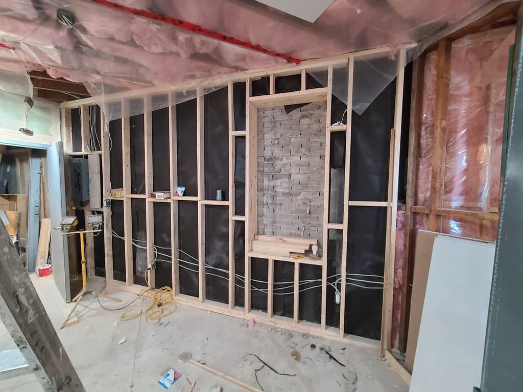Interior framing with wood studs, electrical outlets, and brick wall during renovation