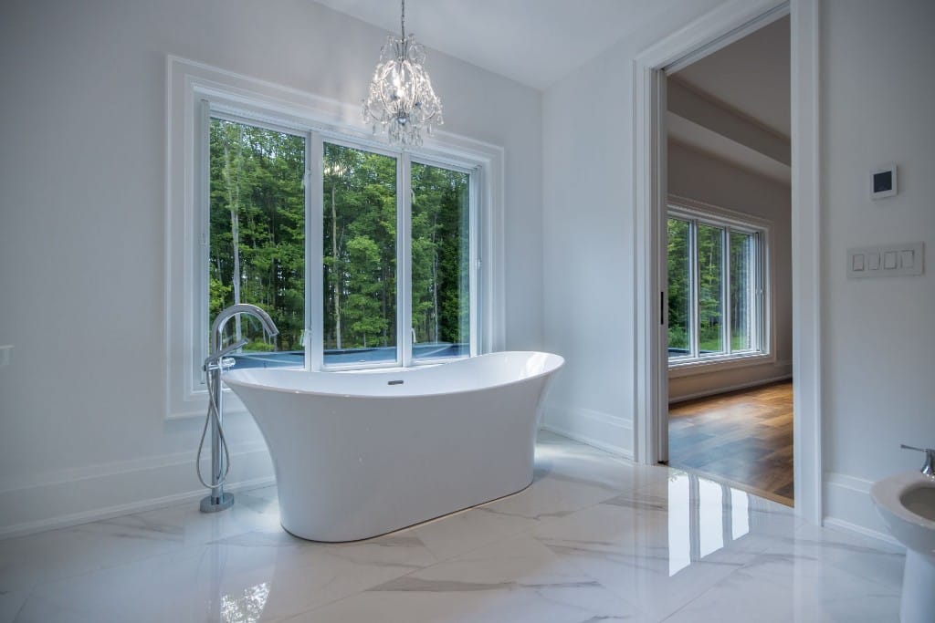 Bright bathroom with a freestanding tub, large window and marble-look floor
