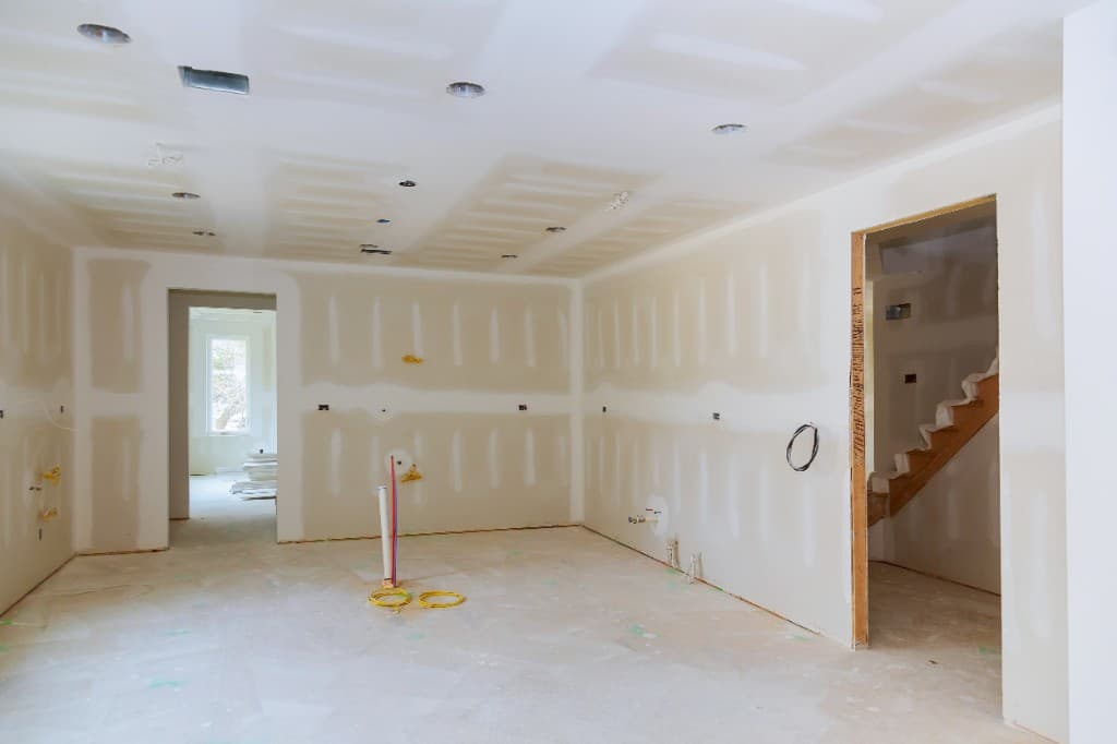Worker installing drywall on vaulted ceiling with scaffolding and insulation visible