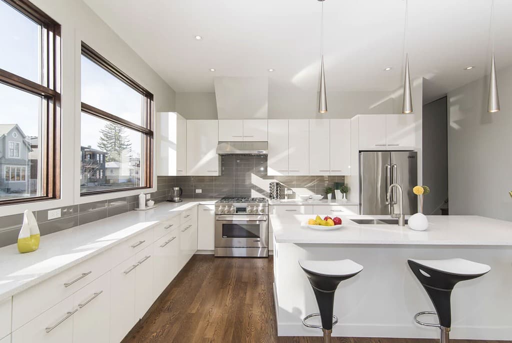 Bright modern kitchen with white cabinetry, island, stainless appliances and pendant lighting